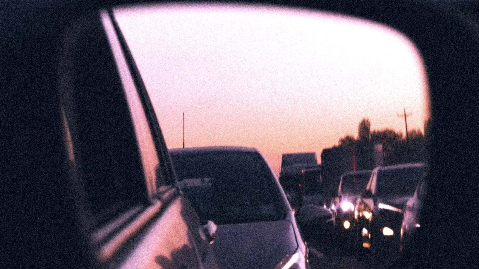 Espejo retrovisor de un vehículo mostrando los autos que circulan detrás al atardecer