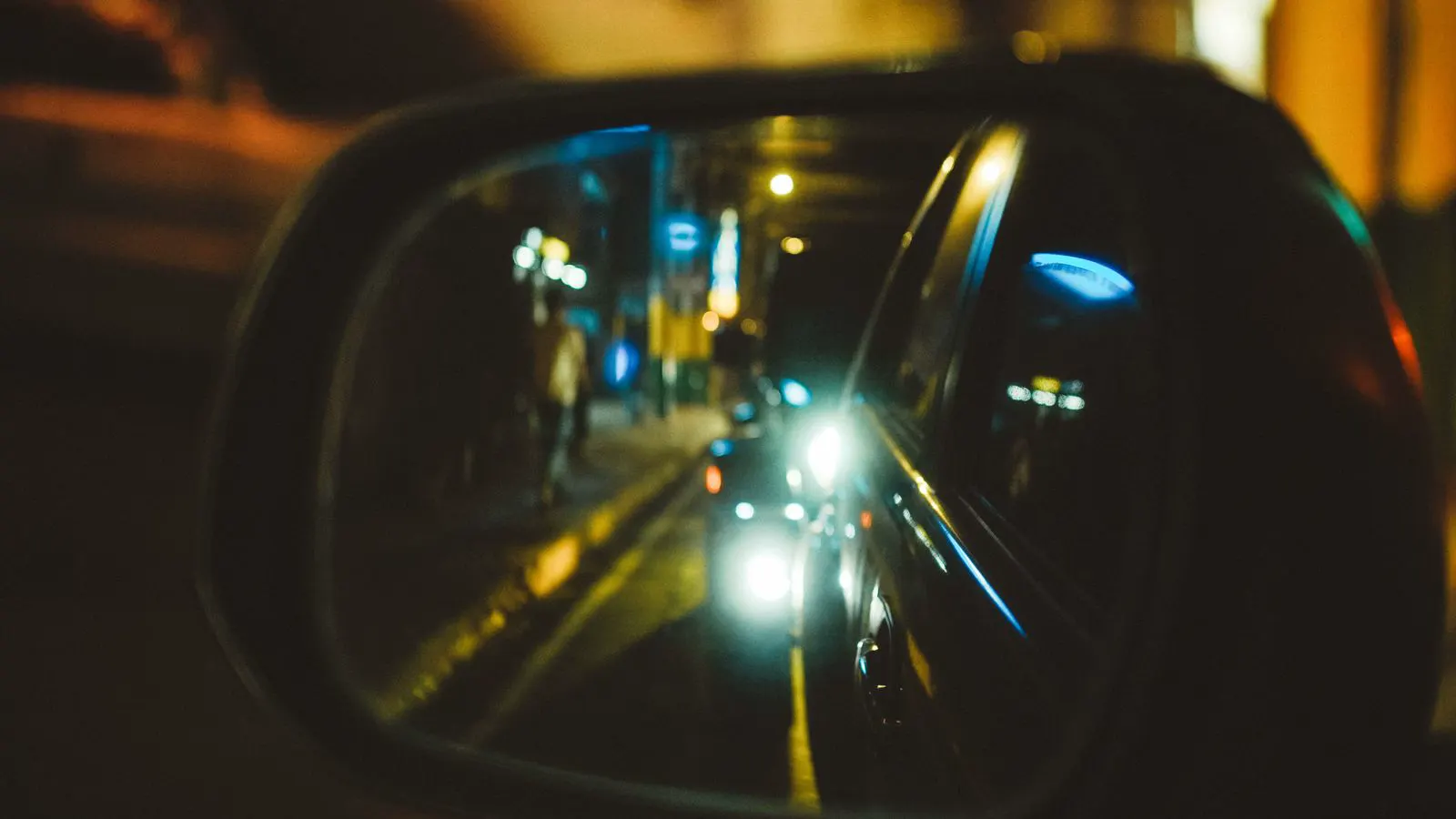 Espejo lateral de un auto de noche reflejando los faros de un vehículo que se acerca por detrás