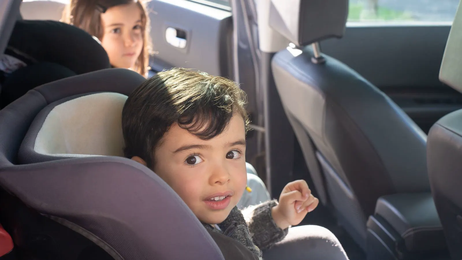 Niño sentado en su silla en el asiento trasero del auto, en un trayecto en familia