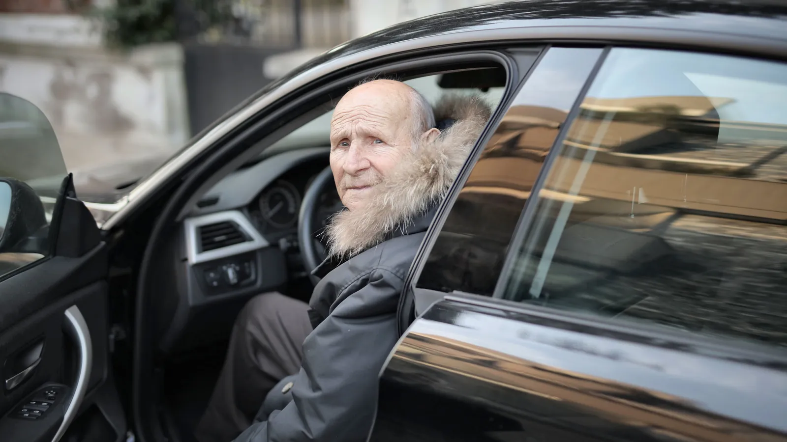 Hombre mayor sentado al volante de su auto con la puerta abierta en la calle