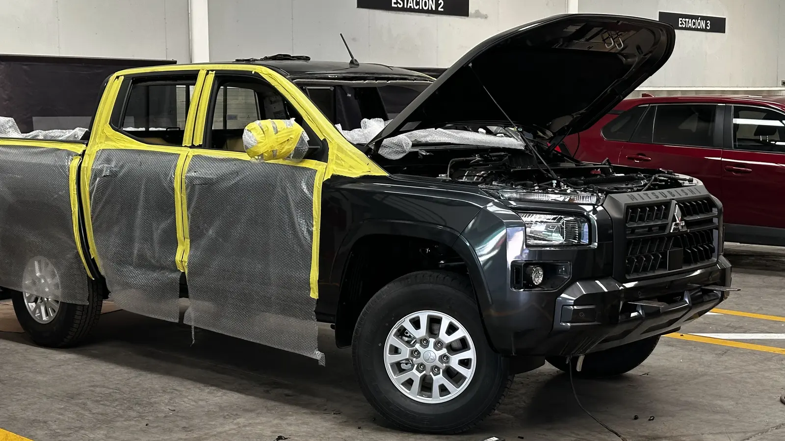 Camioneta doble cabina Mitsubishi L200 en el taller de Blindamax con puertas protegidas y capó abierto durante el proceso de blindaje