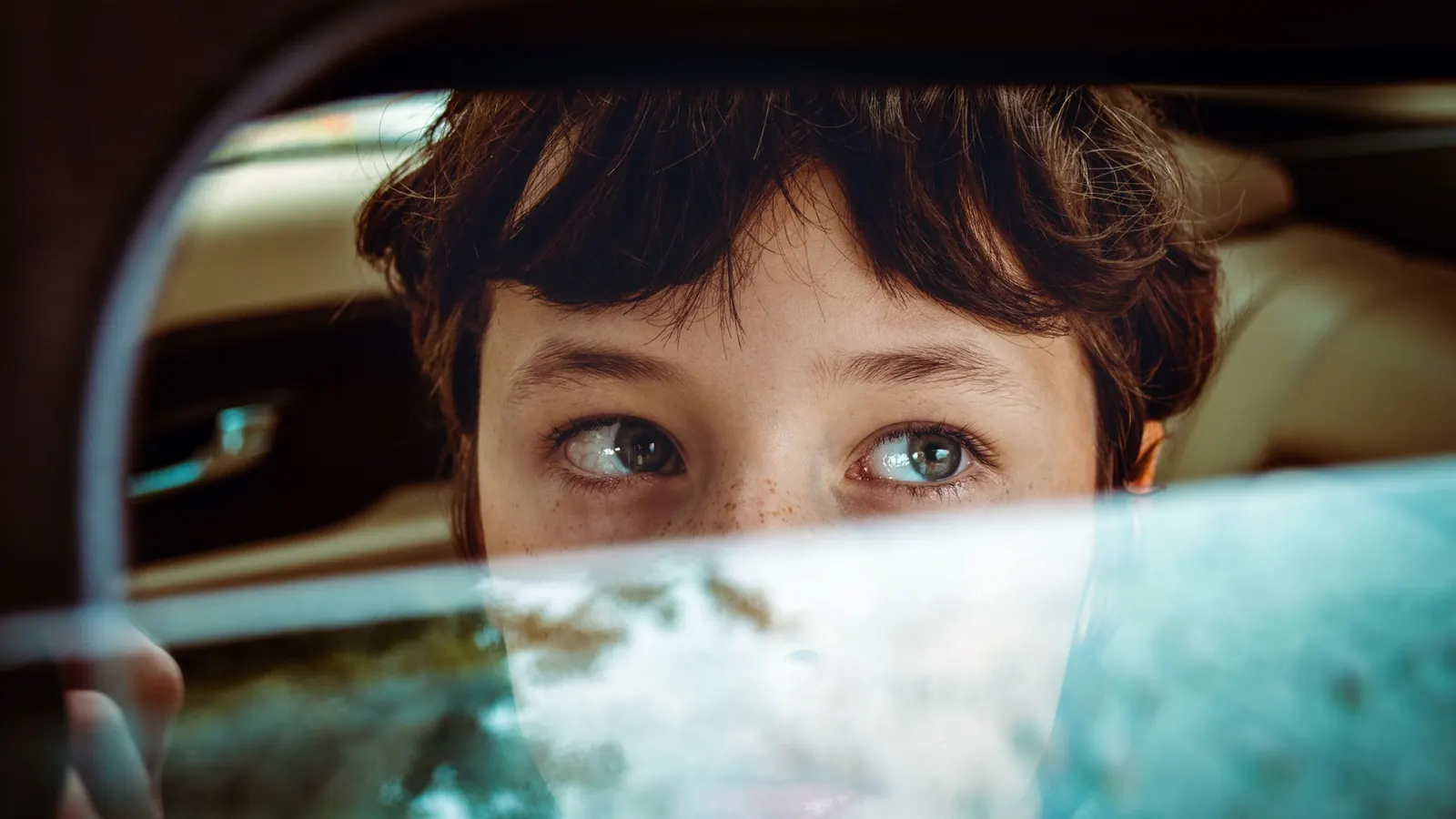 Niño mirando por la ventana de un auto durante el trayecto, visto desde fuera del vehículo