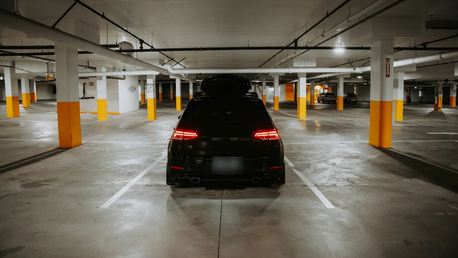 Vehículo oscuro estacionado solo en un estacionamiento subterráneo, con la patente difuminada